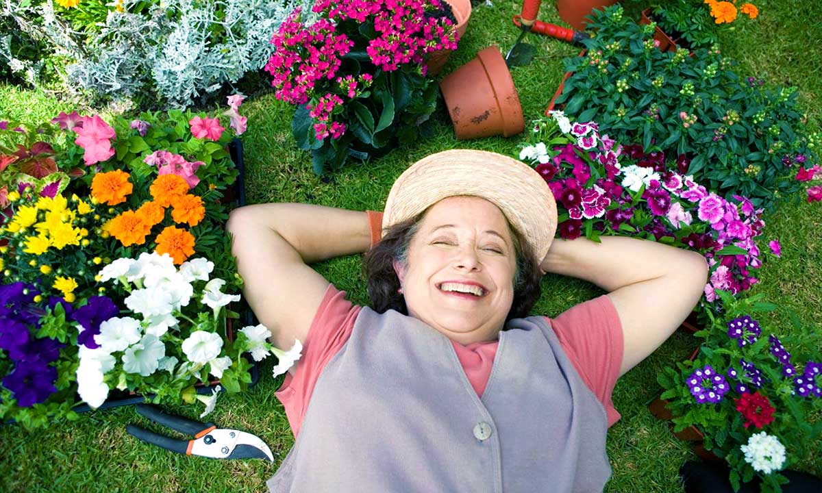 Smiling senior woman laying in garden with surrounded plants 